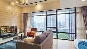 A modern living room with a large TV, comfortable seating, and a city view. - Anggun KLCC Spacious Studio Steps to Monorail & LRT FREE Parking (Kuala Lumpur)