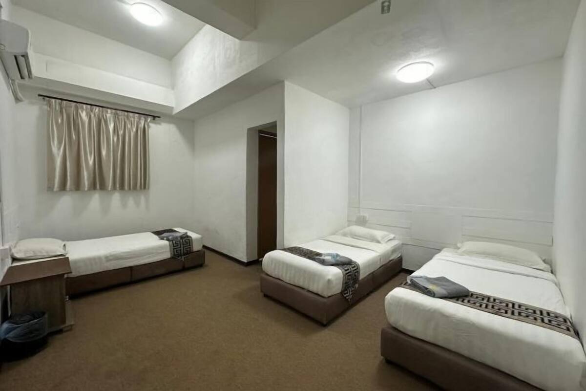 A room with three beds, a small desk, and a window with curtains.