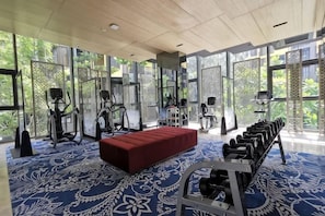 A gym with exercise equipment, a red bench, and large windows. - The Base Central Condominium (Phuket)