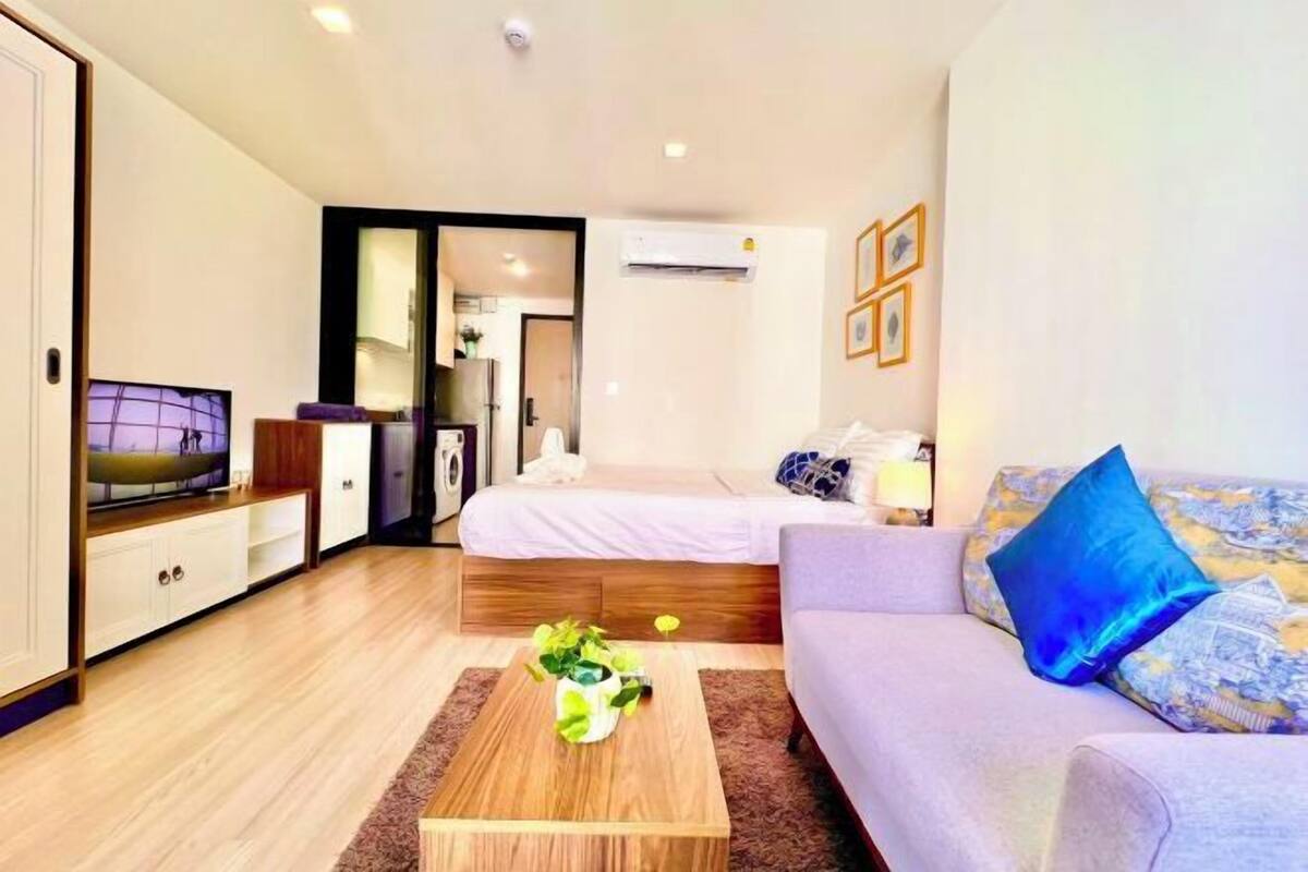 A modern hotel room with a wooden floor, a sofa, a bed, a TV, a coffee table, and a wardrobe.