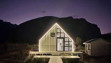 A modern building with a triangular roof, a wooden deck, and a mountain backdrop.