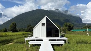 Eine weiße Holzhütte mit einem Satteldach und einer Holzterrasse, mit einem Schild, das anzeigt, dass es sich um ein Bauernhaus handelt.