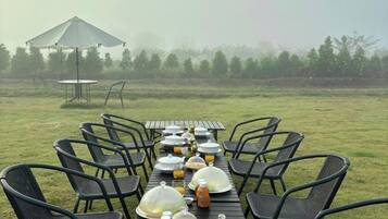 An outdoor dining setup with tables and chairs, a covered umbrella, and a foggy background.