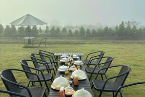 Mobiliario de comedor al aire libre con mesas y sillas, una sombrilla cubierta, y un fondo brumoso.