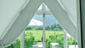 Ein Zimmer mit Blick durch ein dreieckiges Fenster auf eine grüne Landschaft und Berge.