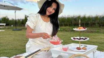 A person sitting outdoors with a guitar, a tray with desserts, and a drink.