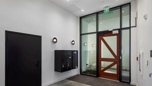 Eine moderne Lobby mit einer schwarzen Tür, einer Glastür mit Holzrahmen und einem wandmontierten Sicherheitspanel.