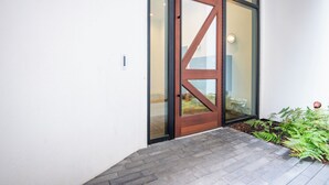 Ein moderner Eingangsbereich mit Holztür und Glasfeldern, einem Ziegelweg und einer kleinen Gartenanlage.