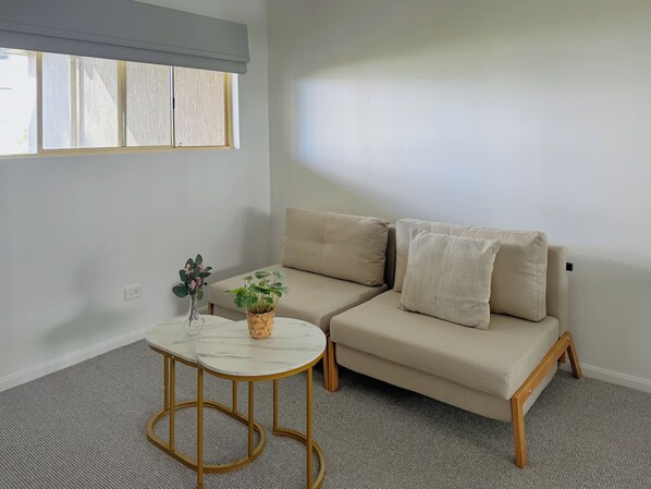 A room with a beige sofa, a small round table, and a window with blinds. - Bridgewater Rivercity (Kangaroo Point)