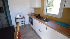A compact kitchen with a microwave, stove, sink, and a window with a view of greenery. - Casa Luisa - Surrounded by greenery, just steps from the sea (Borganzo)