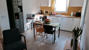 A compact kitchen with white cabinets, a dining table with two chairs, a microwave, and a window providing natural light. - Casa Luisa - Surrounded by greenery, just steps from the sea (Borganzo)