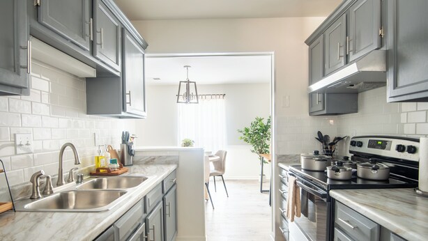 A modern kitchen with grey cabinets, a marble countertop, a built-in oven, and a dining area with a chair and table. - Maple & Marigold – Modern Comfort + WiFi (Birmingham)