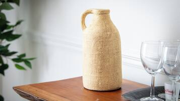 A textured, beige ceramic pitcher on a wooden table with two clear wine glasses beside it.