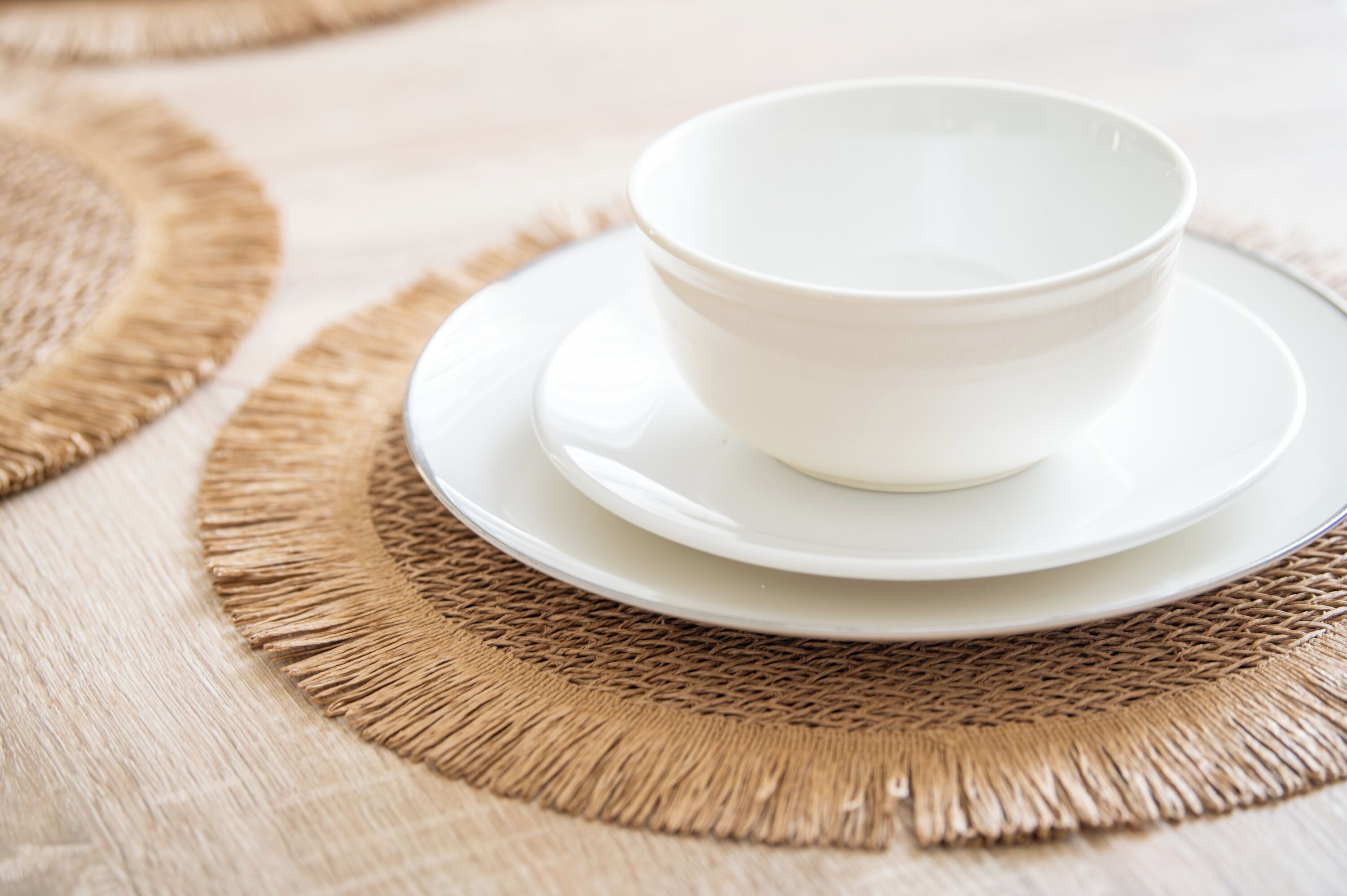 A white bowl on a white plate, placed on a woven placemat.