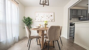 A dining area with a wooden table, four chairs, a vase with flowers, and a painting on the wall. - Maple & Marigold – Modern Comfort + WiFi (Birmingham)