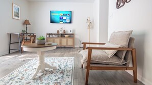 A living room with a TV, wooden furniture, a floral rug, and a wall-mounted artwork. - Maple & Marigold – Modern Comfort + WiFi (Birmingham)