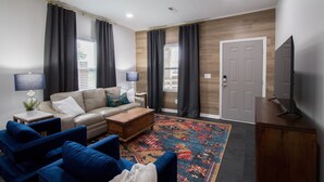 Uma sala de estar moderna com um sofá, poltronas azuis, uma mesa de centro e uma TV em um armário de madeira.