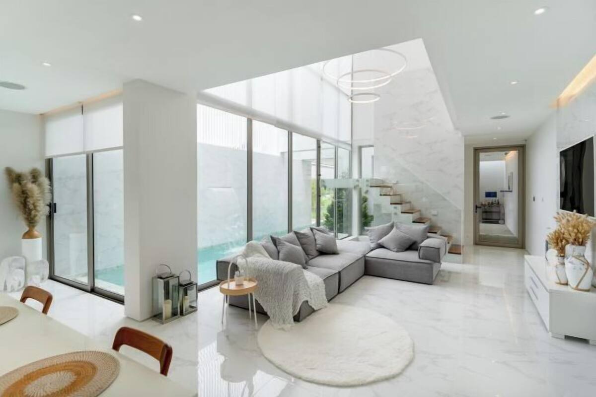 Un intérieur moderne avec une grande porte vitrée, un canapé d’angle gris, un tapis rond et un escalier.