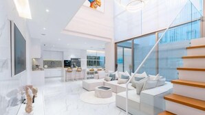 Un interior moderno con una escalera, una zona de estar y una cocina al fondo.