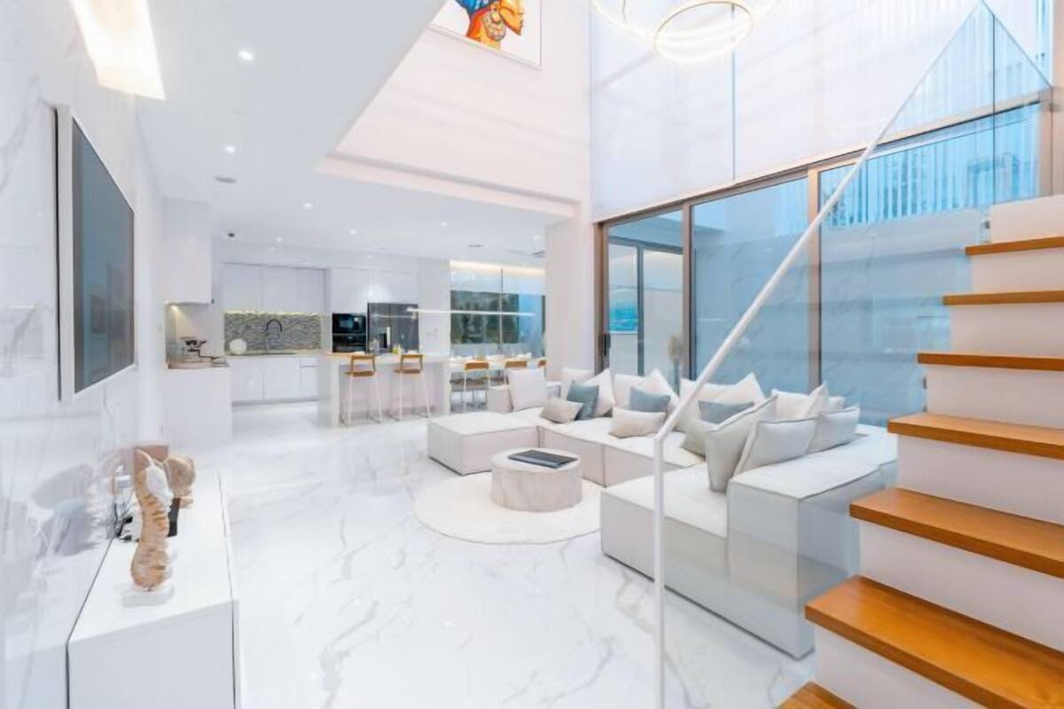 Un intérieur moderne avec un escalier, un coin salon et une cuisine en arrière-plan.