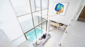 Una sala de estar moderna con un gran ventanal con vistas a una piscina, un sofá con cojines y un comedor.