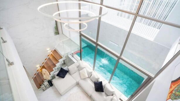 Un interior moderno con un gran ventanal que da a una piscina, un sofá blanco con cojines y una lámpara circular.