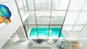 Un interior moderno con piscina envuelta en vidrio, un sofá blanco y una lámpara contemporánea.