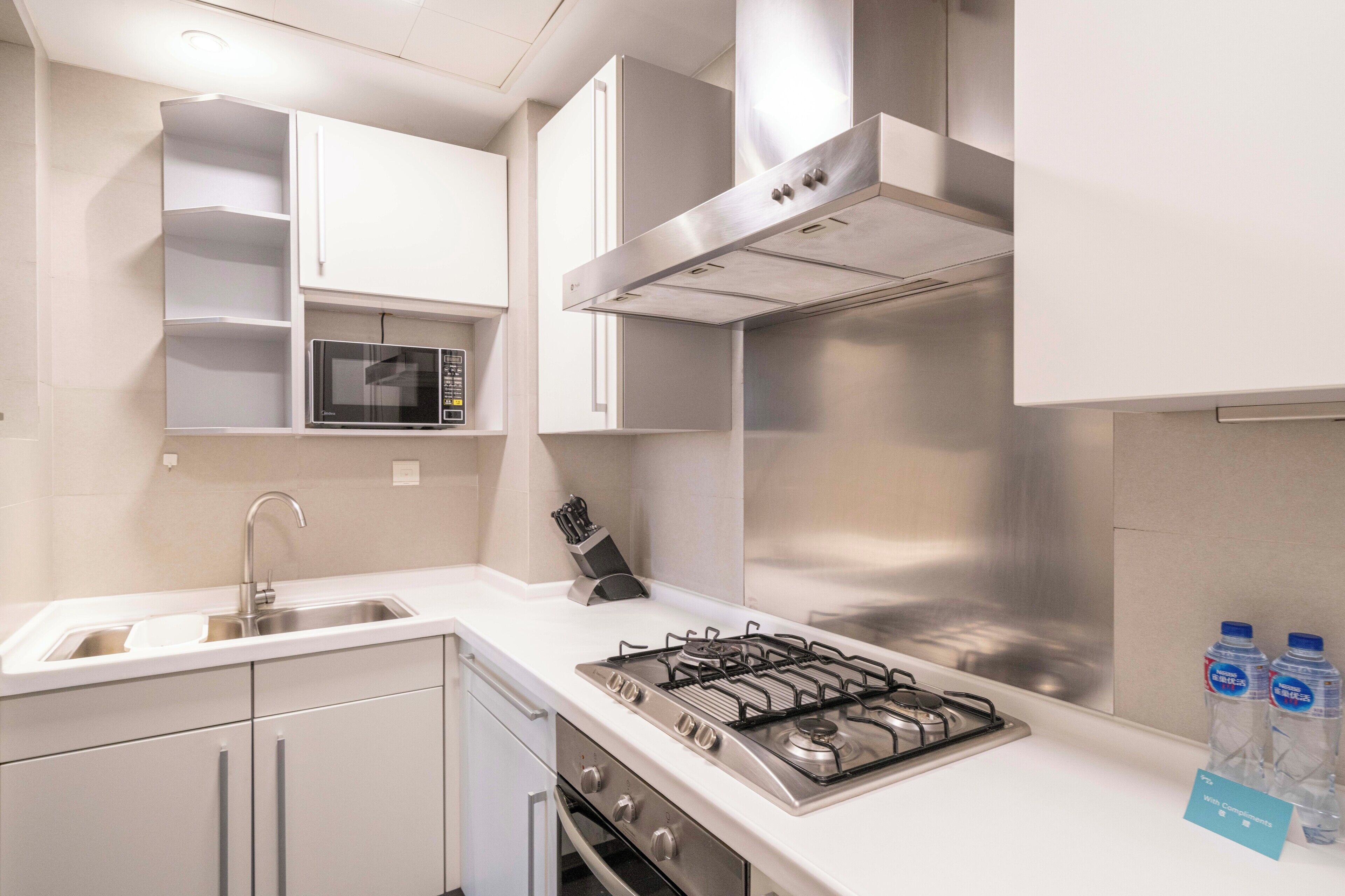 Une cuisine moderne avec des meubles blancs, une hotte en acier inoxydable, un four à micro-ondes encastré et une cuisinière à gaz.