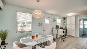 A modern kitchen with white cabinetry, a dining area with a round table and chairs, and a hanging light fixture. - Walk to Ocean! Home w/ Large Yard in Ormond Beach (Ormond Beach)