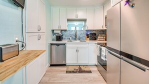 A modern kitchen with white cabinets, a built-in dishwasher, a stainless steel refrigerator, and a coffee maker. - Walk to Ocean! Home w/ Large Yard in Ormond Beach (Ormond Beach)