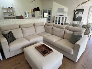 A beige sectional sofa with a patterned pillow, a wooden tray with remote controls, and a white ottoman. - Explore bay and nature in pretty Kostræde Banker (Lundby)