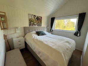 A bedroom with a bed, a nightstand, a dresser, a window with curtains, and a wall-mounted painting. - Explore bay and nature in pretty Kostræde Banker (Lundby)