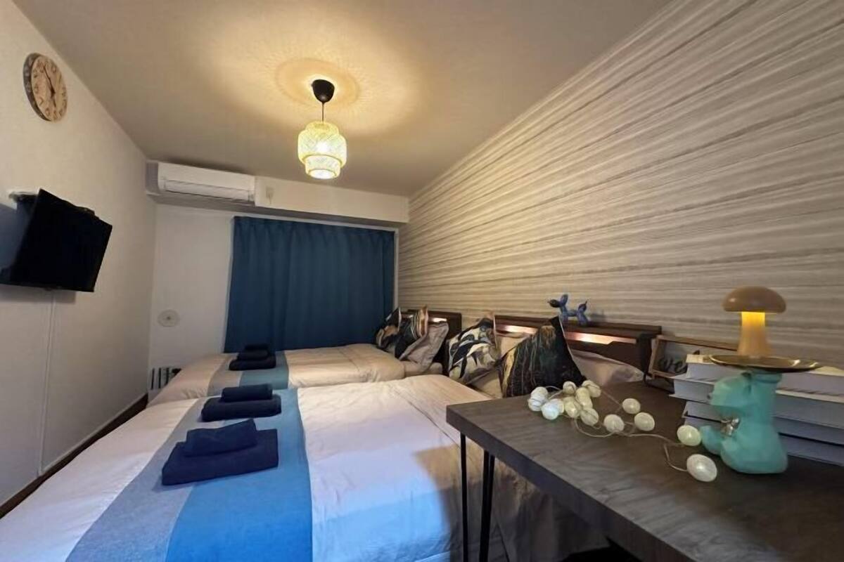 Une chambre d’hôtel avec deux lits, un bureau avec une lampe, une horloge au mur et un rideau.