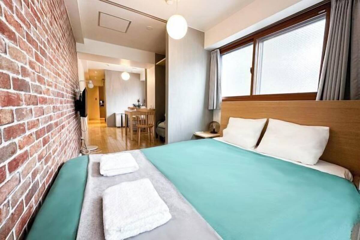 Une chambre d’hôtel avec un mur en briques, un lit recouvert d’une courtepointe verte et donnant sur un espace repas.