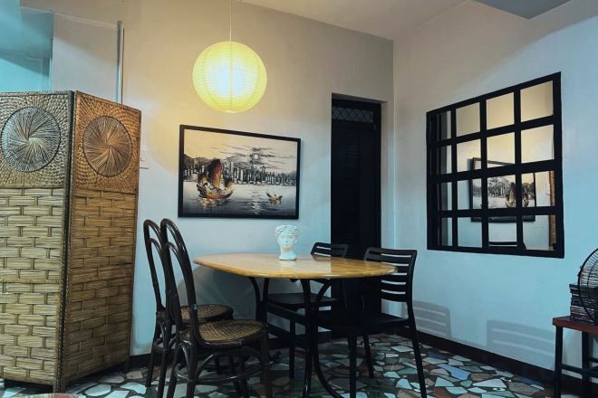 A dining area with a round table, chairs, a hanging light fixture, a framed picture, and a window with a grid pattern.