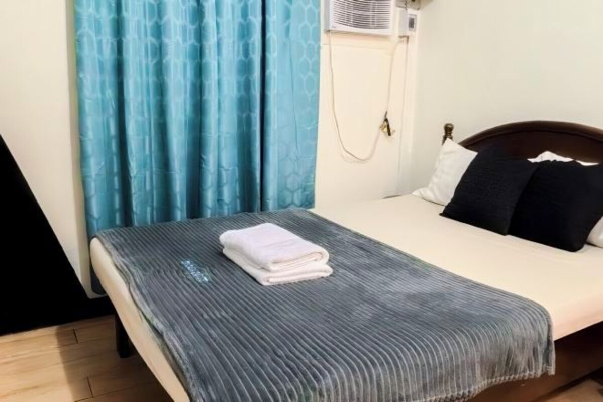 A bed with a white and gray striped blanket, a white pillow, and a dark pillow.