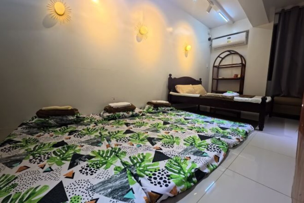 A bedroom with a large bed, a chair, a shelf, and a wall-mounted air conditioner.