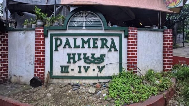 Et skilt med "PALMERA HILLS", med et delvist synligt skilt til en restaurant over det.