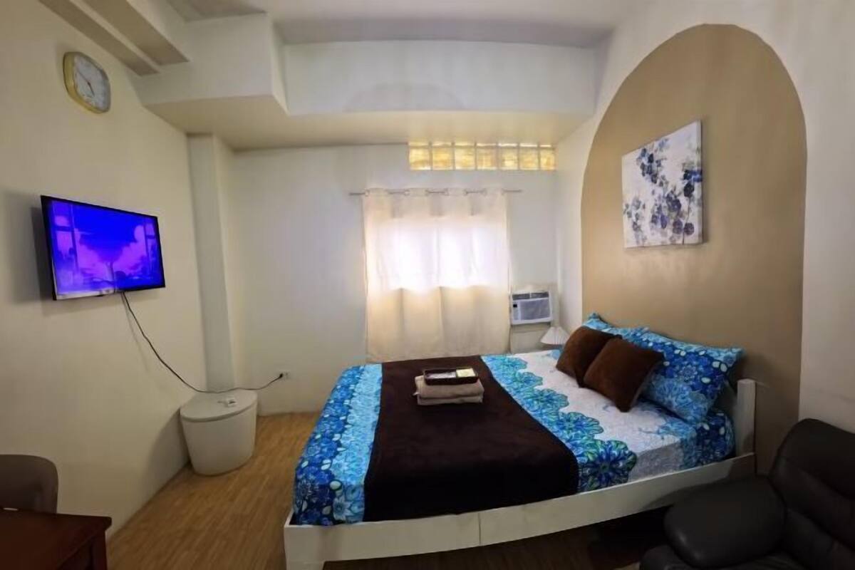Une chambre à coucher avec un lit, une télévision, une horloge et une fenêtre avec des rideaux.