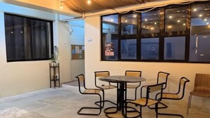 A dining area with a round table and six chairs, a potted plant, and a window with string lights.