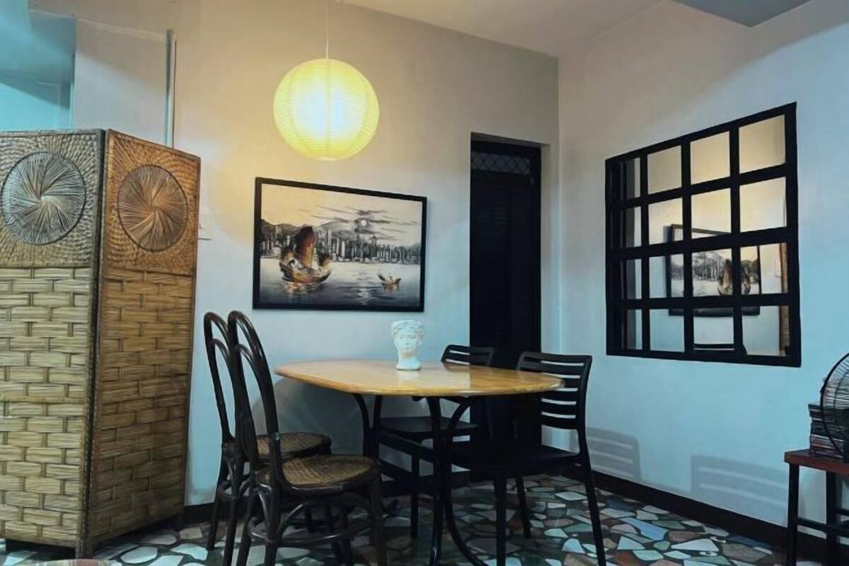 Un espace repas comprenant une table ronde, des chaises, un tableau accroché au mur, une lanterne traditionnelle et un sol à motifs.