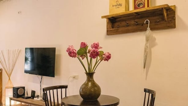 A dining area with a round table, chairs, a vase with flowers, a television, and a wooden shelf with items. - OH Trendy Homes Hoan Kiem LPH - 2 beds - City center (Hanoi)