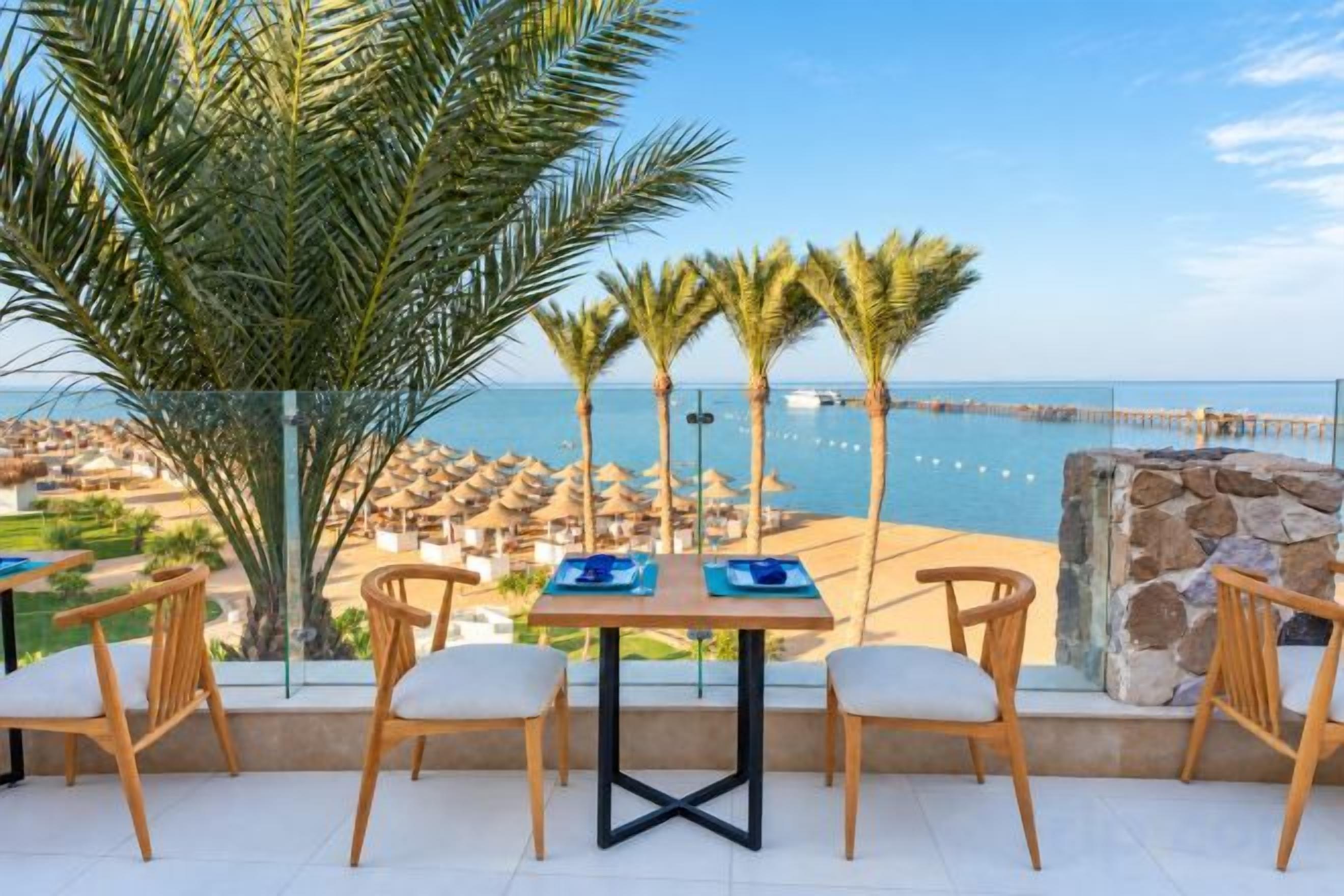 A terrace with a table and chairs overlooking a beach and ocean.