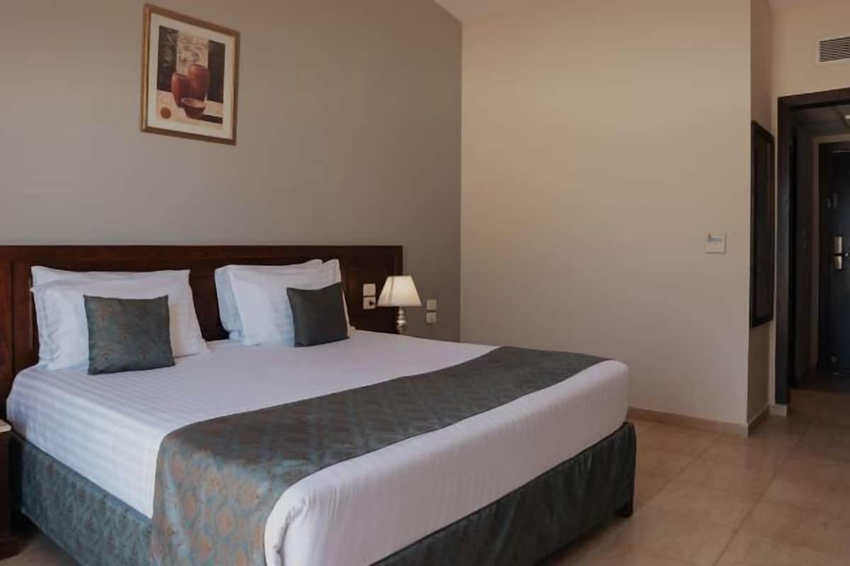 A hotel room with a large bed, a nightstand, a lamp, and a framed picture on the wall.