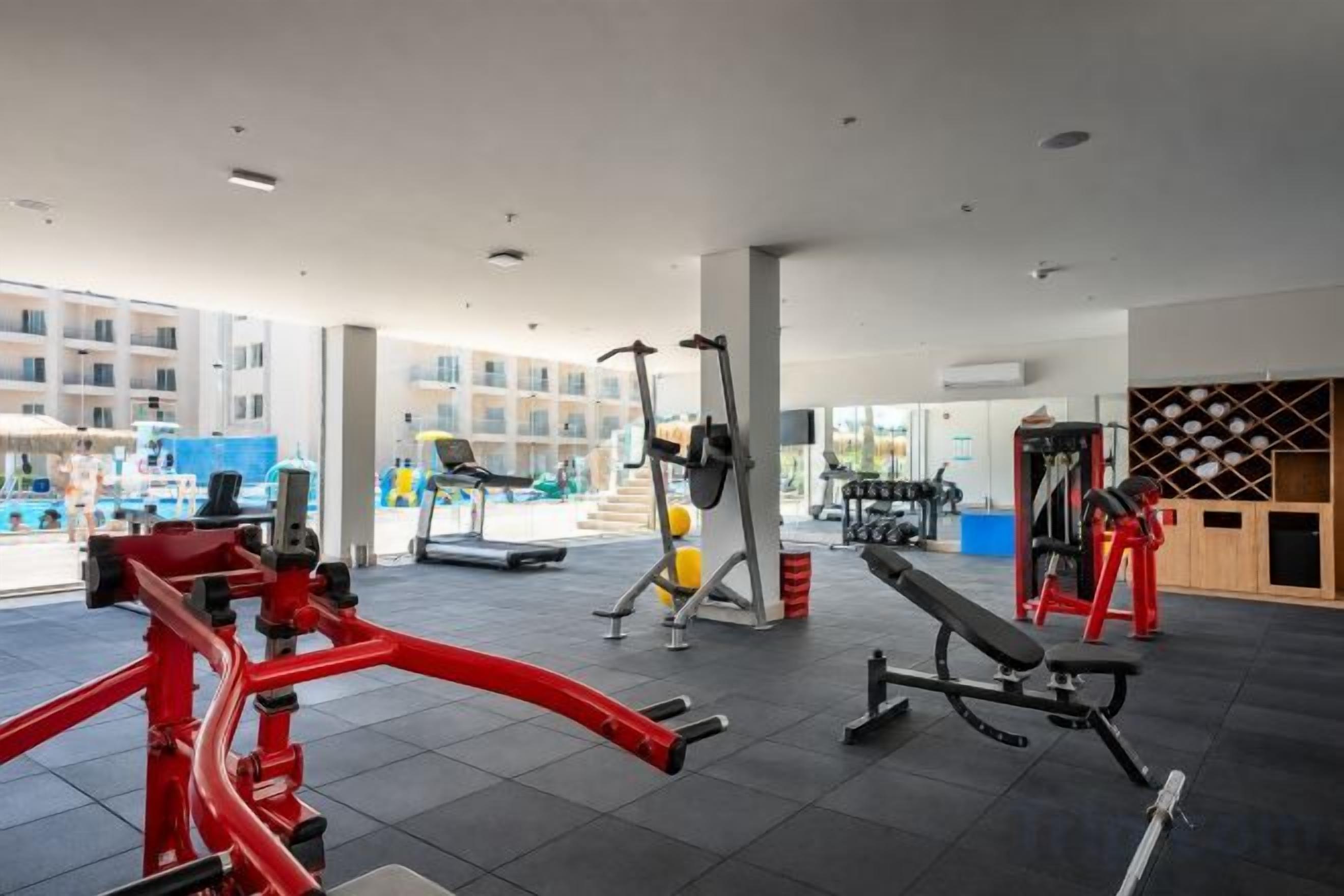 A gym with various exercise equipment, a treadmill, and a view of a building outside.