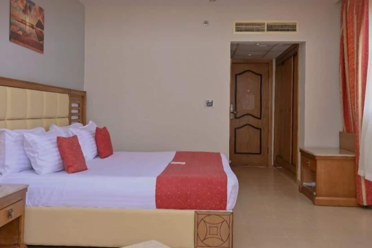 A hotel room with a bed, a nightstand, a wooden door, and a wall-mounted air vent.