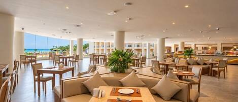 A spacious indoor dining area with multiple seating options, including tables and sofas, and a view of the ocean.