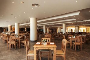 A spacious dining area with multiple tables and chairs, large pillars, and a high ceiling with recessed lighting. - Riviera Aqua Park Resort (Qesm Safaga)