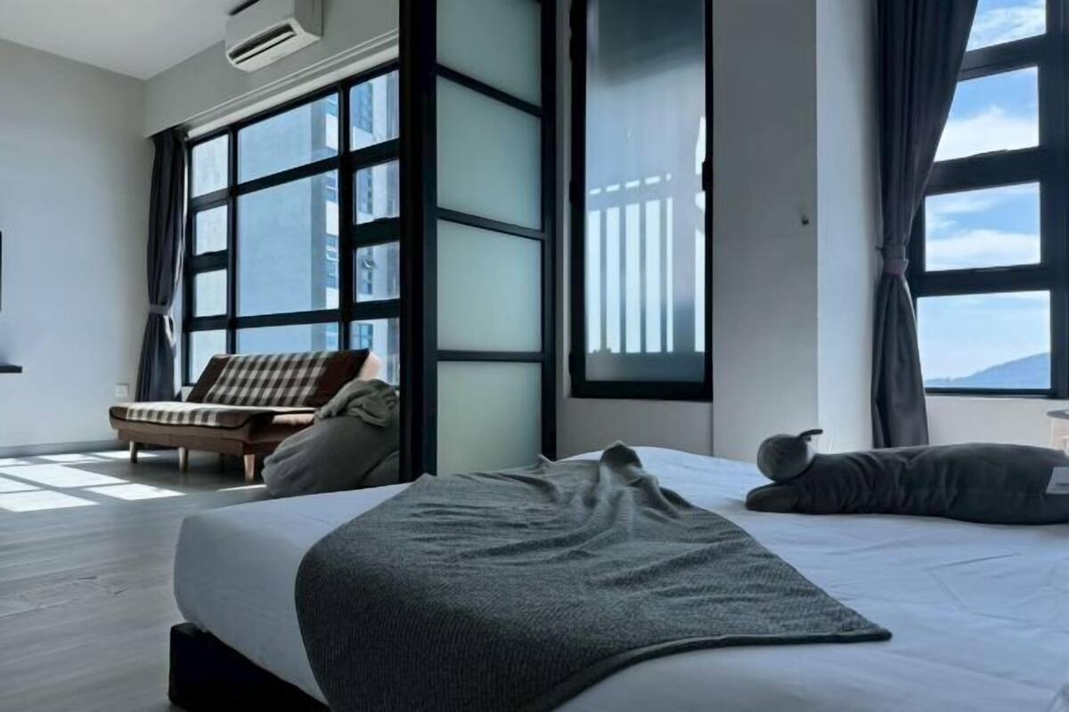 Ein modernes Hotelzimmer mit einem großen Bett, einer Sitzecke und Blick auf die Stadt durch große Fenster.