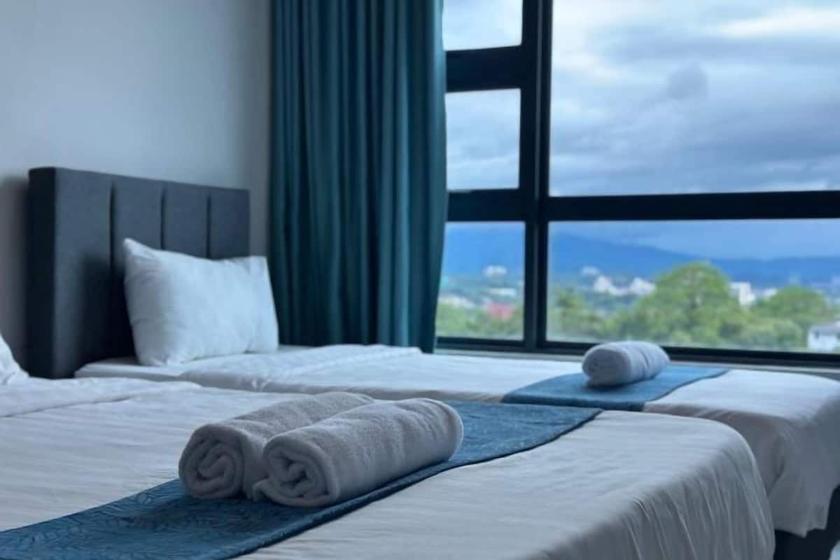 Ein Hotelzimmer mit zwei Betten, einem großen Fenster mit Blick auf die Stadt und einem ordentlich bezogenen Bett mit aufgerollten Handtüchern.